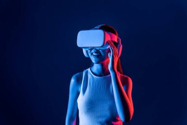 Siberpunk neon ışıklı cihazlarla çevrili zeki bir kadın metaevrene bağlı VR kulaklık takıyor, gelecekçi siber uzay teknolojisi. Zarif bir kadın sanal ortamda yaratılmış gibi görünür. Halüsinasyon.