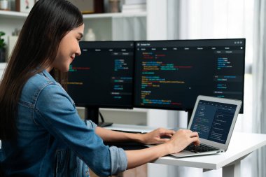 IT geliştiricisinde gülümseyen genç Asyalı dizüstü bilgisayarında kodlama programı verileriyle kotlu tişört giyerek çevrimiçi bilgi yazıyor. Güvenlik analizi iki ekran ile çevrili. Taktik.