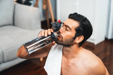Atletik ve sporcu adam spor paspası üzerinde su içiyor. Vücut egzersizlerini bitirdikten sonra evdeki formda ve sağlıklı spor yaşam tarzı için egzersiz yapıyor. Gaiety evde egzersiz eğitimi.