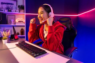 Yüzünde kulaklık renginde kulaklık takan, neon odada online oyun oynayan, Esport meziyetli takım oyuncularına yumruk kaldırarak oynayan güzel Asyalı kız flamasının sunucu kanalı. Taktik.