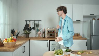 Mutlu baba yemek pişirirken müziğe geçiyor ve modern mutfakta öğle yemeği hazırlıyor. Aktif baba, sebze ve mutfak gereçleri ile çevrili sağlıklı yemek ya da salata yaparken şarkıyla dans ediyor. Pedagoji.