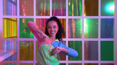 Neşeli İspanyol kız gece kulübünde renkli giysiler giyerken neon ışıkta müzik eşliğinde hareket ediyor. Sokak dansçısı kameraya bakarken hareketli adımlar atıyor. Mutluluk.