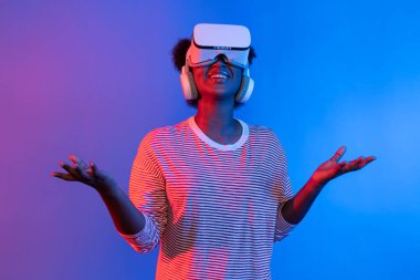 Kullanıcı deneyiminde VR ile sunum yapan genç Afrikalı bir kadın, üç boyutlu teknoloji yenilikçiliği hologram teknolojisi uygulamasındaki çevrimiçi neon stüdyo ışıklandırma arka planı aracılığıyla sunuluyor. Entrika.