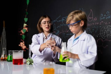 Labaratuvarda yardımcı öğretmen öğrenci laboratuvar önlüğü ve gözlük takıyor ve STEM sınıfında kimya bilimi üzerine deney yapıyorlar. Öğrenci derneği, beher içinde sarı sıvıya indi. Etkinlik.