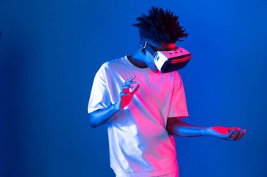 Sanal gerçekliği dijital fütüristik teknolojiye bağlayan pembe mavi neon duvarda VR 'dan bakan genç Afrikalı Amerikalı' ya şaşırdım. Entrika.