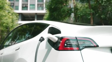 Yavaş çekim EV elektrikli araba yazın yeşil sürdürülebilir şehir bahçesinde şarj oluyor. Kentsel sürdürülebilirlik yaşam tarzı yeşil temiz yeniden şarj edilebilir enerji elektrikli BEV araç iç organları