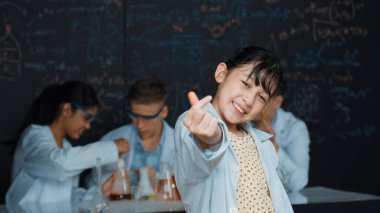 Asyalı bilim adamı çeşitli gruplar deney yaparken minyatür kalbi kameraya gösterdi. Laboratuvarda laboratuvar önlüğü giyerken yazılı kimyasal teorisiyle tahtada duran genç bir öğrenci. Öğretim.