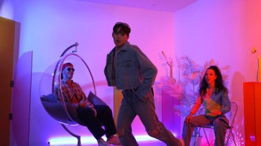 Çok kültürlü bir arkadaş kürsüde otururken Asyalı yetenekli bir dansçı modern müziğe geçiyor. Profesyonel dansçı, hipster takımı tezahürat yaparken ve desteklerken enerjik adımlar atıyor. Mutluluk.