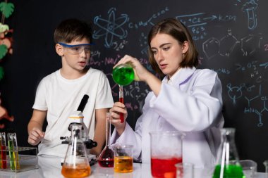 Öğretmen, laboratuarda öğrenciyi destekliyor. Öğrenci ve öğretmen cam kapta sıvı kullanarak STEM sınıfında kimya bilimi üzerine deney yapıyorlar. Karıştırma çözeltisi. Etkinlik.