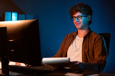 Genç işadamı, Neon Light Modern Ofis 'teki yeni proje surround çalışma masası için kağıt üzerinde tasarım düşünüyor. E-posta ile hediye göndermeden önce not defterine yeni bir iş düşünüyorum. Toplayıcı.