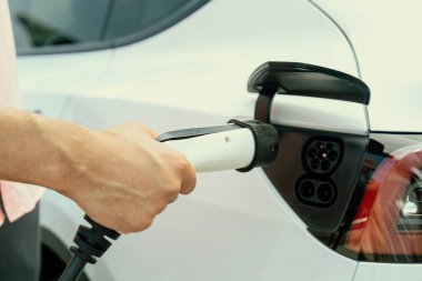 Dışarıdaki şarj istasyonundan EV şarj aletini şarj etmek için elektrikli araca elle tak. Alternatif temiz ve sürdürülebilir enerji kavramına sahip taze gün ışığı ortamı. Kalıcı