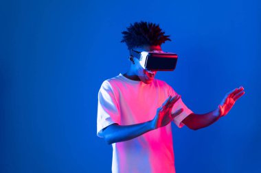 Sanal gerçeklik dünyasını dijital fütüristik teknolojiye bağlayan mavi pembe ışık duvarını gösteren 3 boyutlu hologram gösteren genç bir Afro-Amerikan oyun oyuncusu. Entrika.