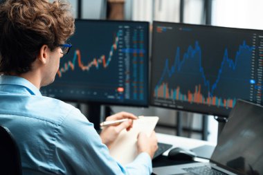 Piyasa stoku grafiği üzerinde çalışan genç profesyonel tüccar ev ofisindeki gerçek zamanlı ekranlara yatırım yaparak önemli döviz kuru kavramları yazarak analiz ediyor. Toplayıcı.