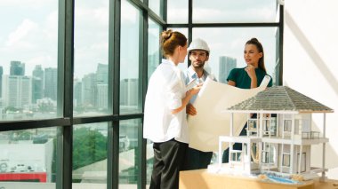 Profesyonel mimar mühendis ekibi konuşuyor, paylaşıyor, tasarım hakkında beyin fırtınası yapıyor. Yönetici planı dinlerken genç mimar plan yapıyor. İzleme