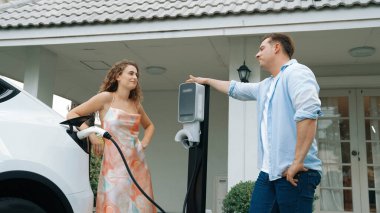 EV şarj istasyonundan çevreci bilinci açık elektrikli araca sahip mutlu ve sevimli bir çift. EV araba teknolojisi gelecekteki sürdürülebilirlik için alternatif ulaşım aracı olarak kullanılıyor. Eşzamanlama