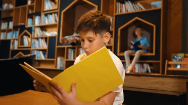 Bir grup zeki öğrenci kütüphanede otururken beyaz çocuk kitap okuyor. Çekici çocuk ders çalışıyor, çocuklar konuşurken romandan ya da kitaptan öğreniyor, eğitim hakkında sohbet ediyor. Etkinlik.