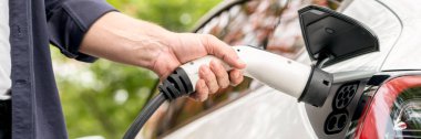 Panorama afişçisi sonbahar gezisi sırasında sonbahar ormanlarında EV arabasının pilini şarj ediyor. Sonbahar tatilinde elektrikli araçla çevre dostu bir seyahat. Yükselt