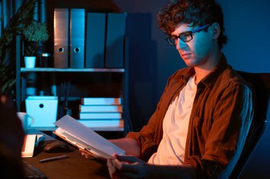 Genç işadamı, Neon Light Modern Ofis 'teki yeni proje surround çalışma masası için kağıt üzerinde tasarım düşünüyor. E-posta ile hediye göndermeden önce not defterine yeni bir iş düşünüyorum. Toplayıcı.