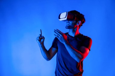 Beyaz adam, neon ışıklı arka planda dururken sanal gerçeklik gözlüğü takıyor. VR gözlüklü kişiler dijital fütüristik yenilik teknolojisini kullanarak metaevrene girerler. Sapma.