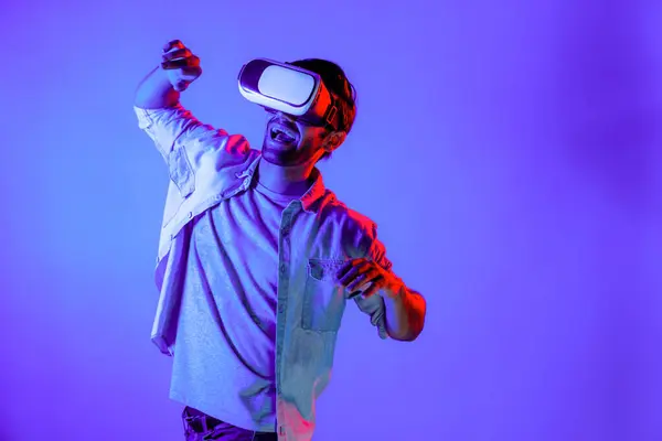 stock image Happy man moving playing volleyball gesture movement while using VR glass at neon background. Caucasian teenager and gamer playing sport game while wearing goggle and innovation technology. Deviation.