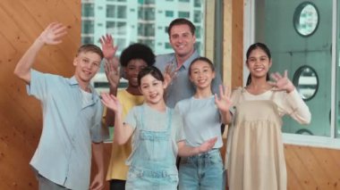 Akıllı öğretmen ve çeşitli öğrenciler kameraya el sallarken ayakta duruyorlar. Farklı ırktan liseli çocukların olduğu yetenekli bir eğitmen. Günlük kıyafetleriyle selamlıyor ve neşeli bir şekilde gülümsüyor. Öğretim