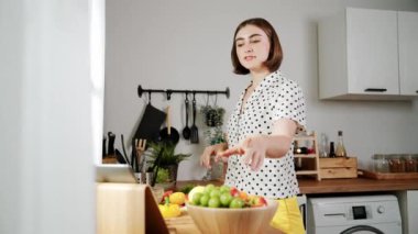 Kafkasyalı anne, modern mutfakta dizüstü bilgisayarda yemek tarifine bakarken salata yapmak için yemek hazırlıyor. Yetenekli ev bekçisi taze sebze kullanarak kahvaltı hazırlıyor. Pedagoji.
