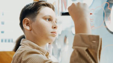 Kafkasyalı yaratıcı öğrencinin yakın çekimi sanat dersinde cam tahtada güzel bir resim çizer. Akıllı çocuk çizim yaparken aynı zamanda çok kültürlü bir arkadaş da çiziyor. Yaratıcılık eğitimi. Etkinlik.