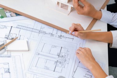 Asyalı kooperatif iş arkadaşı ev modelini ev modeliyle ve bina planıyla birlikte masaya koyarken, profesyonel güzel mimarın el yapımı taslaklarının en üst görüntüsü. Tertemiz..