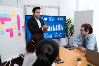 Kutlama jesti ve başarılı takım çalışması yapan bir grup mutlu çoklu etnik iş adamı başarılı satışlar yaptıktan sonra veya toplantı odasında ekranda pozitif finansal veri gösterimi yaptıktan sonra. Habiliment