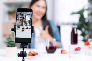 Seçici odaklı akıllı telefon ve gülümseyen genç, güzel Asyalı karışık çilek ve kiraz suyu detoksu değerlendirmesi sosyal medyada sağlıklı ürün tanıtımı sunuyor. Taktik.