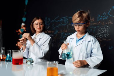 Labaratuvarda yardımcı öğretmen öğrenci laboratuvar önlüğü ve gözlük takıyor ve STEM sınıfında kimya bilimi üzerine deney yapıyorlar. Öğrenci derneği, beher içinde sarı sıvıya indi. Etkinlik.