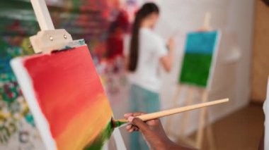 Afrikalı erkek tuvali sıcak tonda boyarken, beyaz elbiseli kız renkli duvarın arkasında havalı renkler çiziyor. Yaratıcı aktivite konsepti. Öğretim