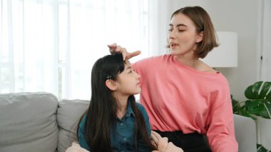 Kafkasyalı anne kızını kucaklıyor ve kanepede oturuyor ve alnından öpüyor. Mutlu anne oturma odasında sevimli Asyalı liseli kıza sevgi ve sevgi gösteriyor. Güzel bir aile birlikte vakit geçirir. Pedagoji.