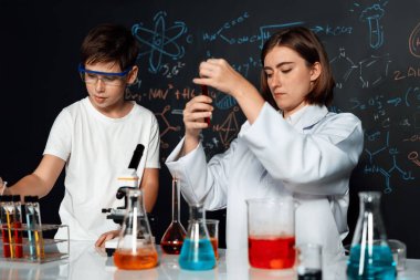 Öğretmen, laboratuarda öğrenciyi destekliyor. Öğrenci ve öğretmen cam kapta sıvı kullanarak STEM sınıfında kimya bilimi üzerine deney yapıyorlar. Karıştırma çözeltisi. Etkinlik.