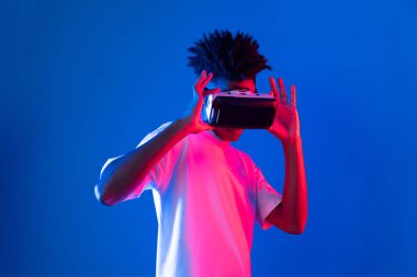 Sanal gerçekliği dijital fütüristik teknolojiye bağlayan pembe mavi neon duvarda VR 'dan bakan genç Afrikalı Amerikalı' ya şaşırdım. Entrika.