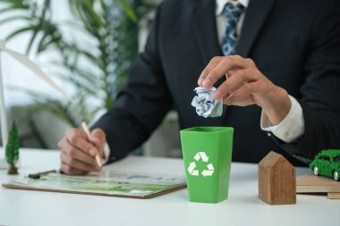 İşadamı, daha yeşil bir çevre ve sıfır kirlilik için geri dönüşüm yaparak şirketlerin çevre dostu atık yönetimi üzerindeki çabalarını sembolize eden küçük geri dönüşüm kutusuna kağıt atığı koydu. Döngü