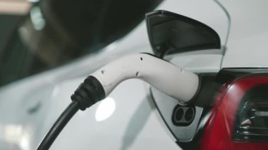Yavaş çekim yakın EV elektrikli araba şarj istasyonunda fişe takılı, şehir merkezindeki alışveriş merkezinin otoparkında şarj bataryasını şarj ediyor. Elektrikli araç iç organları için temiz yeşil sürdürülebilir enerjisi var.