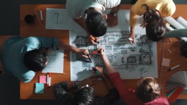 İnşaat mühendisi ekibinin renkli paletlerle toplantı masasında yazı yazması. Yönetici proje planlarına bakarken bir grup farklı insan plan yapıyor ve not alıyor. Sempozyum.