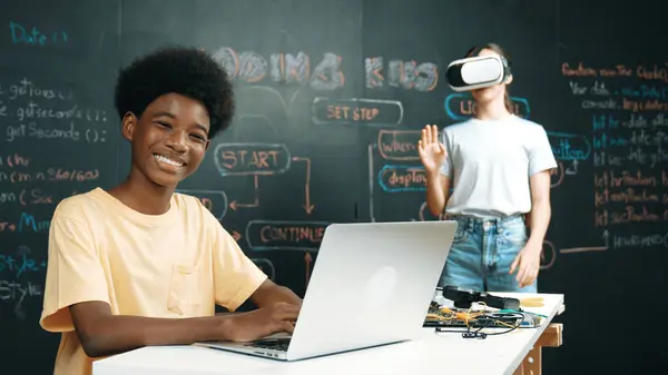 stock image Smart african student programing and coding innovative system while caucasian girl enter in metaverse or virtual world by using VR or head set at blackboard in STEM technology classroom. Edification.