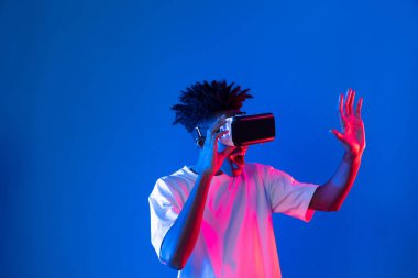 Sanal gerçeklik dünyasını dijital fütüristik teknolojiye bağlayan mavi pembe ışık duvarını gösteren 3 boyutlu hologram gösteren genç bir Afro-Amerikan oyun oyuncusu. Entrika.