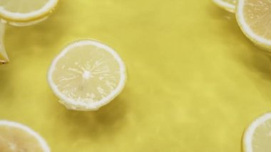 Dalgalı su yüzeyinde limon dilimleri. Sarı arka planda ve su dalgasında dilimlenmiş limon dilimini kapat. Doğal ışık. Makro. Tazelik ve susuzluk kavramı. Poster için tasarım, tebrik kartı. Pabulum.