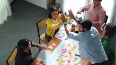 Yaratıcı başlangıç ekibinin takım çalışmalarını veya başarılı projelerini teşvik etmek için beşlik çakarken, aynı zamanda not ve yapışkan notlar kullanarak iş akışını yönetmek için yoğun bir görev tahtası yapmasının en üst görünümü. Cemaat.