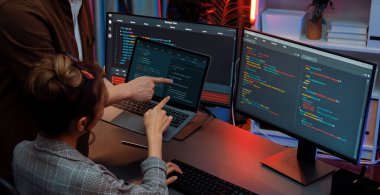 Modern ofisteki neon ışık odasında bilgi ağını gösteren dizüstü bilgisayarla iki ekranda veri çalıştıran akıllı web sitesi geliştirme kodlayıcı sistemini tartışan IT geliştiricilerinin ciddiyeti. İnfobahn.