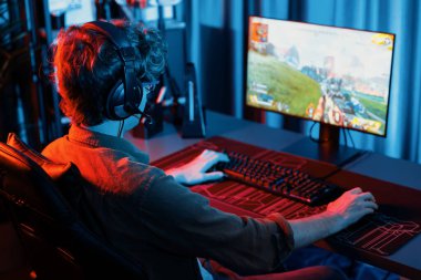 Genç oyun flamasının sunucu kanalı, takım oyuncusu, dijital neon odasında mikrofonlu kulaklık takarak bilgisayar ekranında çoklu oyuncuyla savaş oyunu oynuyor. Toplayıcı.