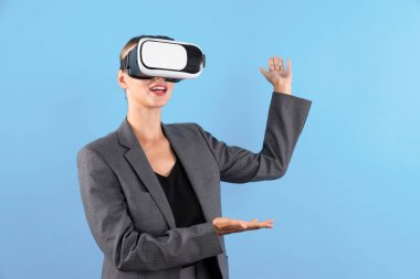 Sanal gerçeklik gözlüklü bir iş kadını mavi arka planda dururken kendine güvenen bir fikirle karşınızda duruyor. Profesyonel proje yöneticisi elinde bir şey tutarken takım elbise giyiyor. Teknoloji. Kısıtlanma.