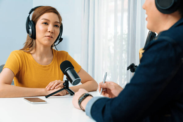 Улыбающийся радиоведущий, одетый в наушники, берёт интервью у женщины-оратора, делясь информацией со слушателями на онлайн-сайте социальных сетей. Инфобан.