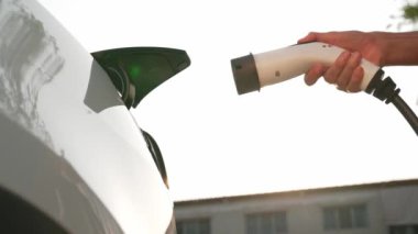 Genç adam, alışveriş merkezinin otoparkındaki EV otomobil şarj istasyonunda elektrik için akıllı telefon kullanıyor. EV aracıyla modern çevre ve sürdürülebilir kentsel yaşam tarzı