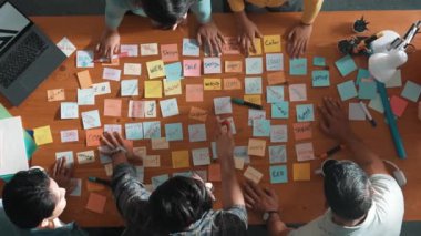 Top view of business team giving high five to celebrate project while standing at table with sticky notes and laptop. Aerial view of designer clapping hands to congratulate successful idea. Symposium.