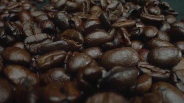 Karışık aromalı kahve çekirdeği yığını masaya saçılmış ve kavrulmuş kahve çekirdekleri etrafa saçılmış siyah arkaplanla çevrilmiş. Makrografi. Ağır çekim. Pabulum.