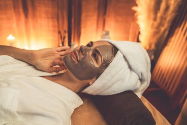 Kaplıca salonunun sakin atmosferi, üst düzey kadın müşteri sıcak mum ışığında kömür kömürü yüz kremi masajıyla kendini yenilemeye çalışıyor. Yüz bakımı ve güzellik konsepti. Sessiz.